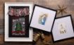 A rustic wood surface displays framed holiday art, including festive house rules, a nativity scene, and a church. Brass bells and gold star decor accent the cozy Christmas arrangement.
