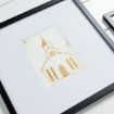 A framed, minimalist gold and white print of a church with a steeple and arched windows, displayed on a white background.