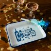 A white tray with blue trim reading "CHEERS" in stylized letters, next to a blue party horn, two glasses of pink champagne, and gold confetti on a wooden table.