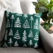 A green throw pillow with white tree patterns rests on a light gray sofa. A fuzzy white blanket is draped over the sofa arm, and a leafy potted plant is visible in the background.