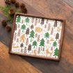 A wooden tray with a white surface featuring illustrations of green trees and brown woodland animals, including a bear, fox, deer, and rabbit, placed on a rustic wooden table with pinecones and greenery nearby.