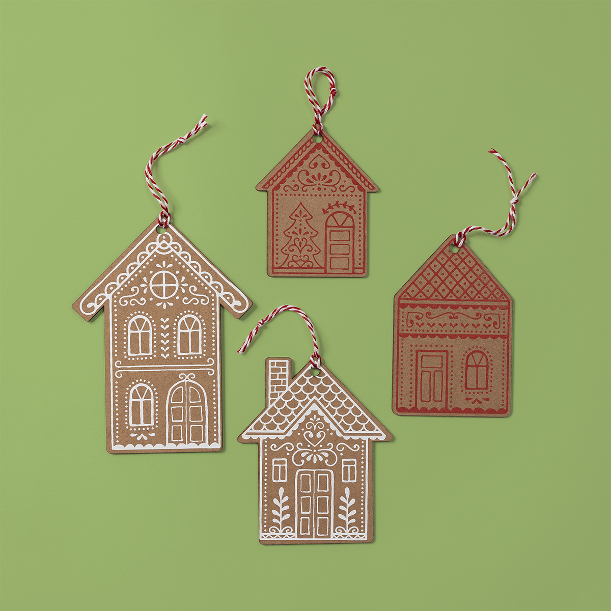 Four gingerbread house-shaped ornaments with white icing-like designs and red-and-white string loops are arranged on a light green background.