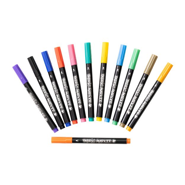 Twelve colorful fabric markers arranged in a semicircle, with one orange marker placed horizontally in front. Each marker has a black body and a colored cap matching the ink color.