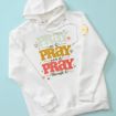 A white hoodie with the phrase "Pray on it, pray over it, pray through it" in pastel green, yellow, and red letters, decorated with heart and flower doodles, laid flat on a light blue background.