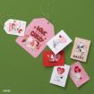 Assorted Snoopy-themed Valentine's Day cards and tags with red, pink, and white designs are arranged on a green background. The cards feature Peanuts characters and various love messages.