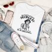 Flat lay of a white T-shirt with a vintage cartoon woman and the text “Don’t just be part of the problem. Be the whole problem.” Surrounded by sunglasses, jeans, a phone, lipstick, jewelry, a jacket, and white sneakers.