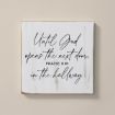 A white wooden sign with cursive black text that reads: "Until God opens the next door, praise Him in the hallway." The background is a light beige wall.