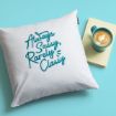 A white pillow with teal text reading "Always Sassy, Rarely Classy" rests next to a closed yellow book and a teal mug of latte, all placed on a light blue background.