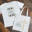 A white t-shirt with floral designs and the words "His Grace is sufficient." lies next to a white tote bag featuring a beige cross and the same phrase. Both are displayed on a wooden floor.
