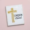 A white canvas with a gold wooden cross on the left and the words "CHOSEN AND Loved" in black script on the right, set against a pale pink background.