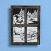 A framed artwork resembles a window, showing a black-and-white winter scene with a snowman, pine trees, a river, and a sled, set against a solid light blue background.
