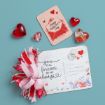 A decorated Valentine’s postcard with a red and pink bow, a card that says "Happy Valentine’s Day", and four heart-shaped decorations are arranged on a blue background.