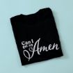 A folded black t-shirt with the phrase "Can I get an Amen" printed in bold, white script letters on the front, placed on a light blue background.