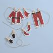 Paper cutouts of Santa Claus's clothes—jacket, hat, pants, mittens, socks—hang from string with tiny clothespins on a light blue background, resembling a festive clothesline.