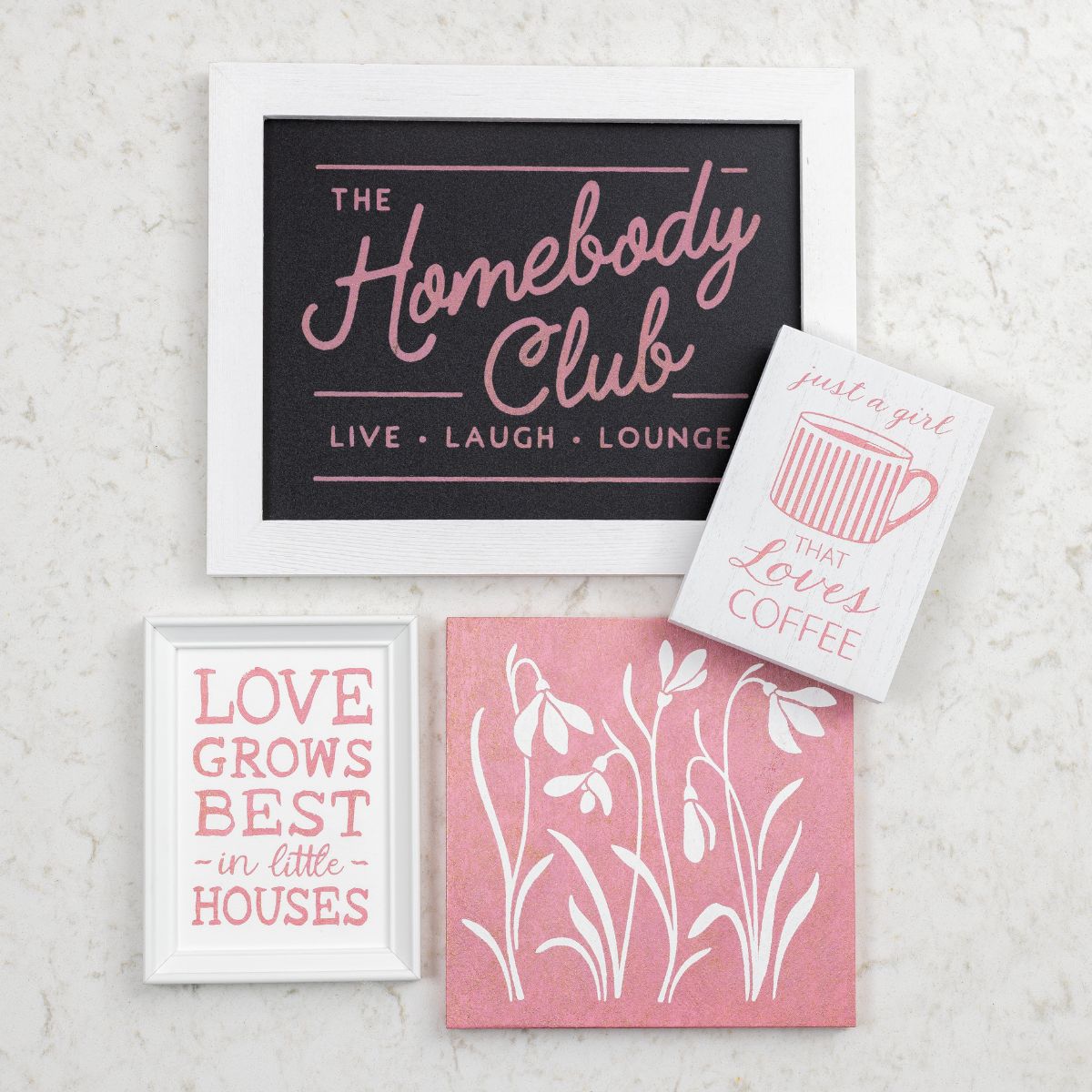 Four decorative wall art pieces: one says "The Homebody Club - Live. Laugh. Lounge.", one shows a coffee cup with "just a girl that loves coffee," one says "LOVE GROWS BEST in little HOUSES," and one has white flowers on pink.