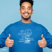 A smiling man wearing a blue sweatshirt with a graphic of Charlie Brown and the text "MY ANXIETIES HAVE ANXIETIES. – Charlie Brown" gives two thumbs up against a blue background.