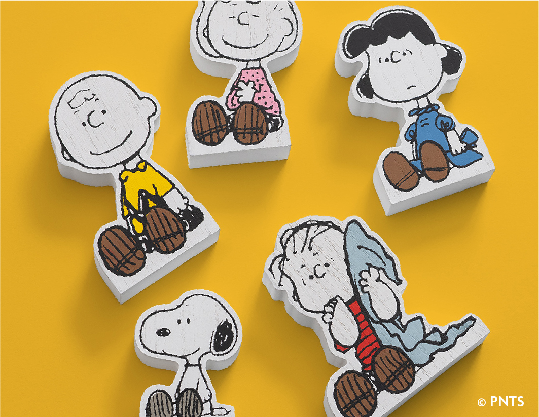 Five illustrated Peanuts character cutouts—Charlie Brown, Snoopy, Linus, Lucy, and Sally—lie scattered on a bright yellow background.
