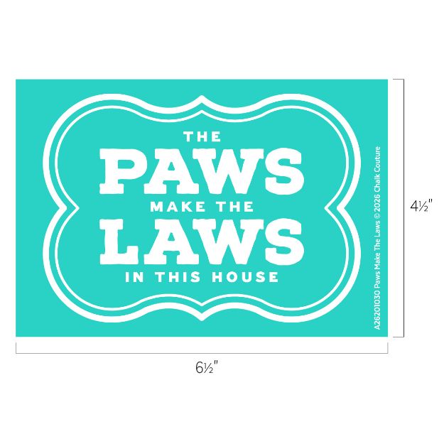 A teal sign with white text reads, "The PAWS make the LAWS in this house." The dimensions are 6½ inches wide and 4½ inches tall.