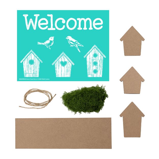 A craft kit including a "Welcome" sign with birdhouses and birds, three blank house-shaped cutouts, a rectangular piece of cardboard, green moss, and a piece of twine, all laid out on a white background.