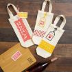 Three decorated wine tote bags with cheerful tags and patterns sit beside a wooden cutting board labeled “Great minds drink alike” and a bottle of rosé, all arranged on a wooden surface.