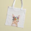 A white tote bag featuring a watercolor illustration of a rabbit wearing a colorful floral crown, placed on a light beige background.