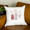 A white throw pillow with a watercolor-style print of three vintage vases holding wildflowers, placed on a brown leather chair. A small potted plant sits in the background.
