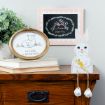 A wooden table holds books, a framed sheep drawing with the text "The Lord is my Shepherd," a bunny cutout holding a carrot, and a framed illustration of a bunny with "Happy Easter" text, next to a leafy plant.