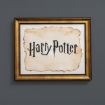A gold-framed picture displays the words "Harry Potter" in bold, stylized black letters on an old, weathered parchment background, set against a dark gray wall.