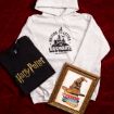 A flat lay of Harry Potter merchandise on red velvet: a gray hoodie with "Waiting for my letter to Hogwarts" print, a black T-shirt with "Harry Potter" logo, and a framed illustration of the Sorting Hat on books.