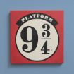 A square sign with a red border and a white center displays "PLATFORM 9 3/4" in bold black text, referencing the magical train platform from the Harry Potter series, set against a blue wall.
