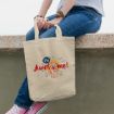 A person wearing blue jeans and pink sneakers sits on a ledge, holding a beige tote bag that features a cartoon mouse and the text "Be Awesome!" in colorful letters.