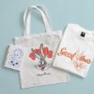 A white tote bag with a Bugs Bunny graphic and logo, a white T-shirt reading "Good vibes" with an outline of Bugs Bunny, and a notebook featuring a blue line drawing of Tweety on a light blue background.