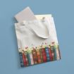 A white tote bag with handles lies on a blue surface. The bag features a colorful print of old books with flowers growing between them. Two books, one light gray and one yellow, peek out of the bag.