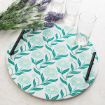 A round serving tray with a teal floral pattern and black handles sits on a white surface near three empty glasses and a bunch of lavender flowers.