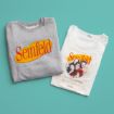 Two folded T-shirts on a teal background: one gray with the Seinfeld logo, and one white with the Seinfeld logo and a photo of the main cast from the TV show, arranged in a heart shape.