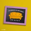 A framed sign with a purple border displays an orange couch illustration and the text “I’d rather be watching FRIENDS” on a black background, set against a bright yellow surface.