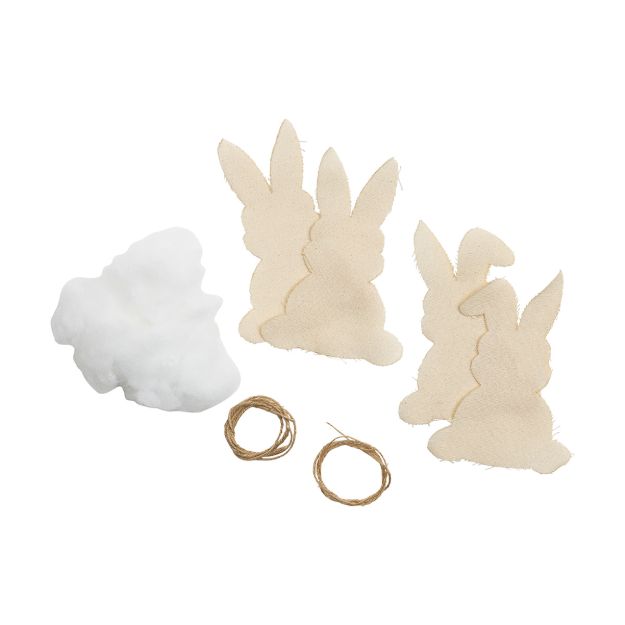 Three beige fabric cutouts shaped like bunnies, a pile of white stuffing, and two small loops of brown twine are arranged on a white background.