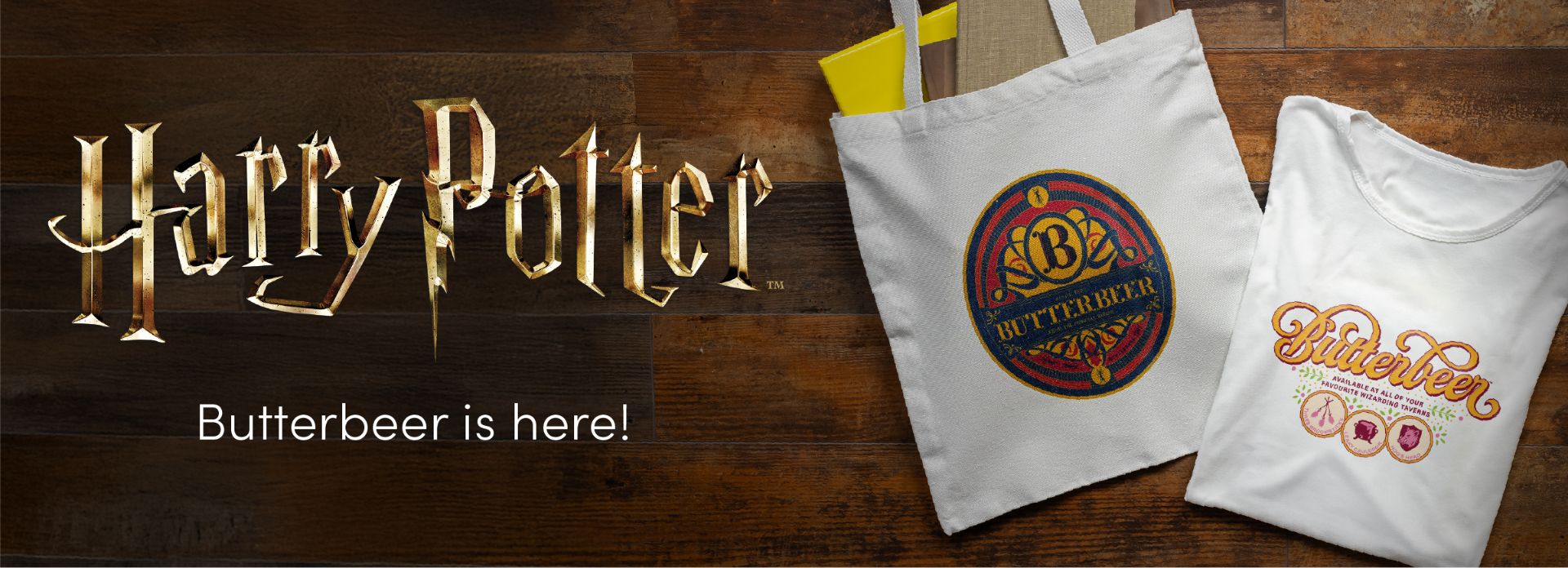 White tote bag and T-shirt with colorful Butterbeer-themed Harry Potter designs on a wooden surface. Large “Harry Potter” logo and the text “Butterbeer is here!” appear on the left.