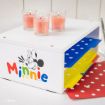 A white organizer decorated with Minnie Mouse and colorful "Minnie" text holds yellow, blue, and red folders with white polka dots. Three pink candles in glass holders are on top. Red polka dot paper lies beside the organizer.