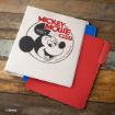 A white Mickey Mouse Club binder featuring Mickey Mouse’s face is stacked on top of blue and red file folders on a rustic wooden surface.