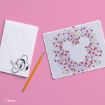 A notepad with Donald Duck illustration, a yellow pencil, and a white mouse pad with a large Mickey Mouse head surrounded by colorful mini Mickey heads, all on a pink background.