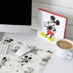A desktop with an iMac, mouse, and keyboard on a Disney-themed mouse pad featuring classic cartoon characters, a cup of coffee, and a standing artwork of Mickey Mouse in red shorts and yellow shoes.