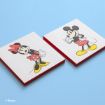 Two square wooden plaques on a light blue surface feature illustrations of Minnie Mouse and Mickey Mouse, each wearing their classic red, white, and yellow outfits.