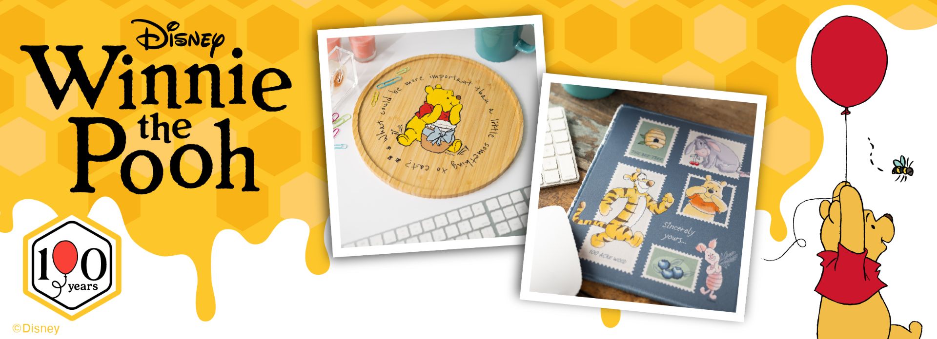 Banner featuring Disney’s Winnie the Pooh. Left: “Disney Winnie the Pooh” text and a 100 years logo. Center: image of a Pooh mousepad and a cross-stitch pattern book. Right: Pooh holding a red balloon with a bee nearby.