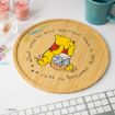 A round wooden board with a drawing of Winnie the Pooh sitting on a honey pot, surrounded by the quote: "What could be more important than a little something to eat?" Office supplies and a keyboard are nearby.