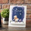 A decorative stand displays an illustration of Winnie the Pooh and Piglet gazing at the night sky, with stars, a crescent moon, and the words “Shine bright.” A potted plant is nearby, set against a brick wall.