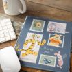 A mousepad featuring Winnie the Pooh characters—Tigger, Eeyore, Piglet, and Pooh—along with themed stamps and images, sits on a wooden desk next to a keyboard, mouse, and a mug.