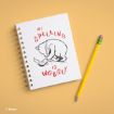 A spiral notebook with a drawing of Winnie the Pooh holding a piece of paper and the words "My spelling is wobbly" written in red, next to a yellow pencil on a light orange background.
