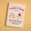 A spiral-bound notebook with a beige cover featuring Winnie the Pooh pulling a cart of honey and red text that reads "Pooh's Farm, Hundred Acre Quality, Since 1925, 100 Acre Wood, The Honey Division, Manufactured." © Disney.