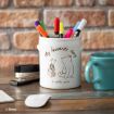 A white mug with drawings of Winnie the Pooh and Piglet holds colorful pens and markers. The mug says, "My favourite story is with you." Nearby are a stapler, a blue mug, a mouse, and a keyboard on a wooden desk.